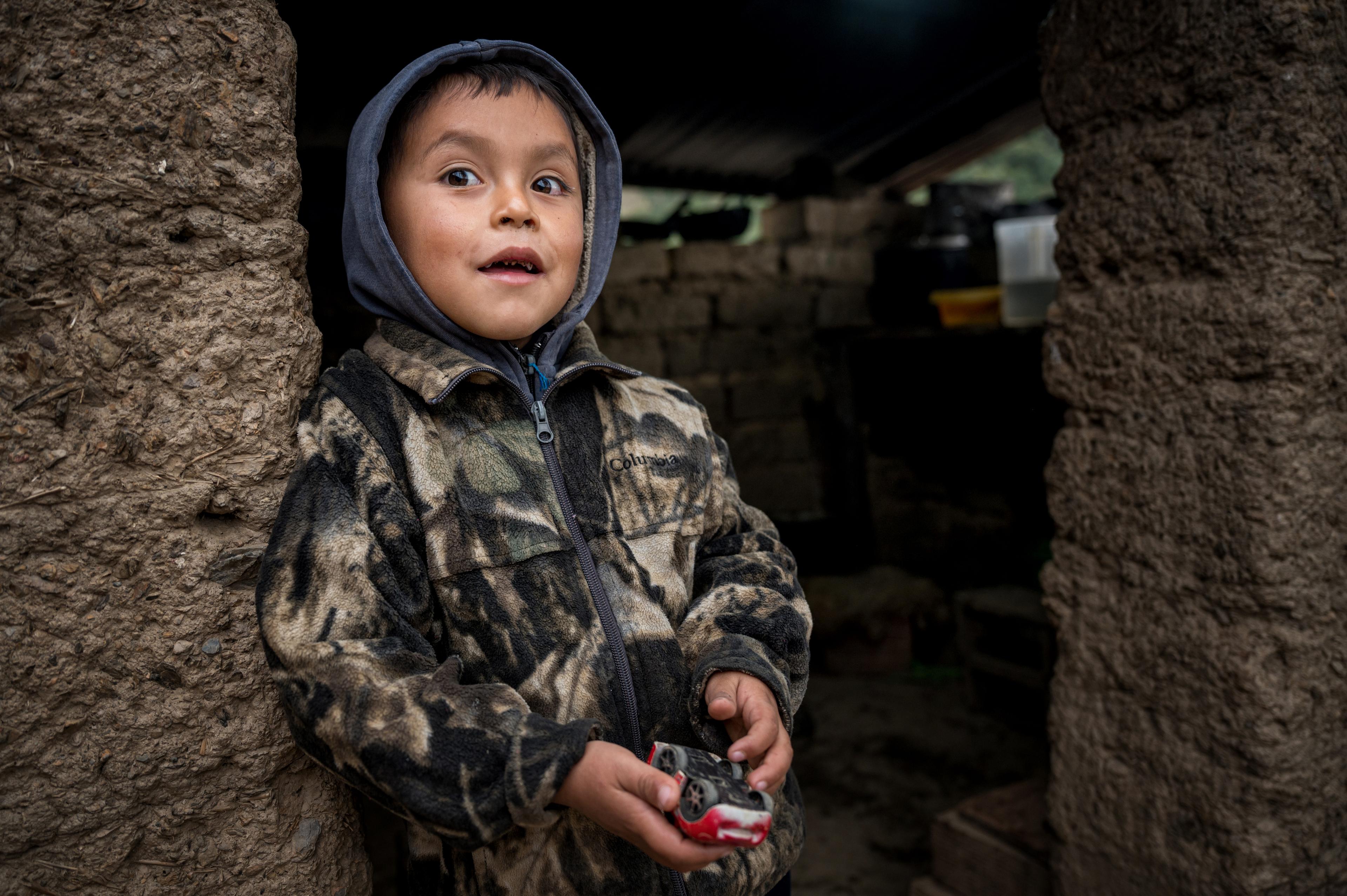 A smiling little boy stands before a stone wall.