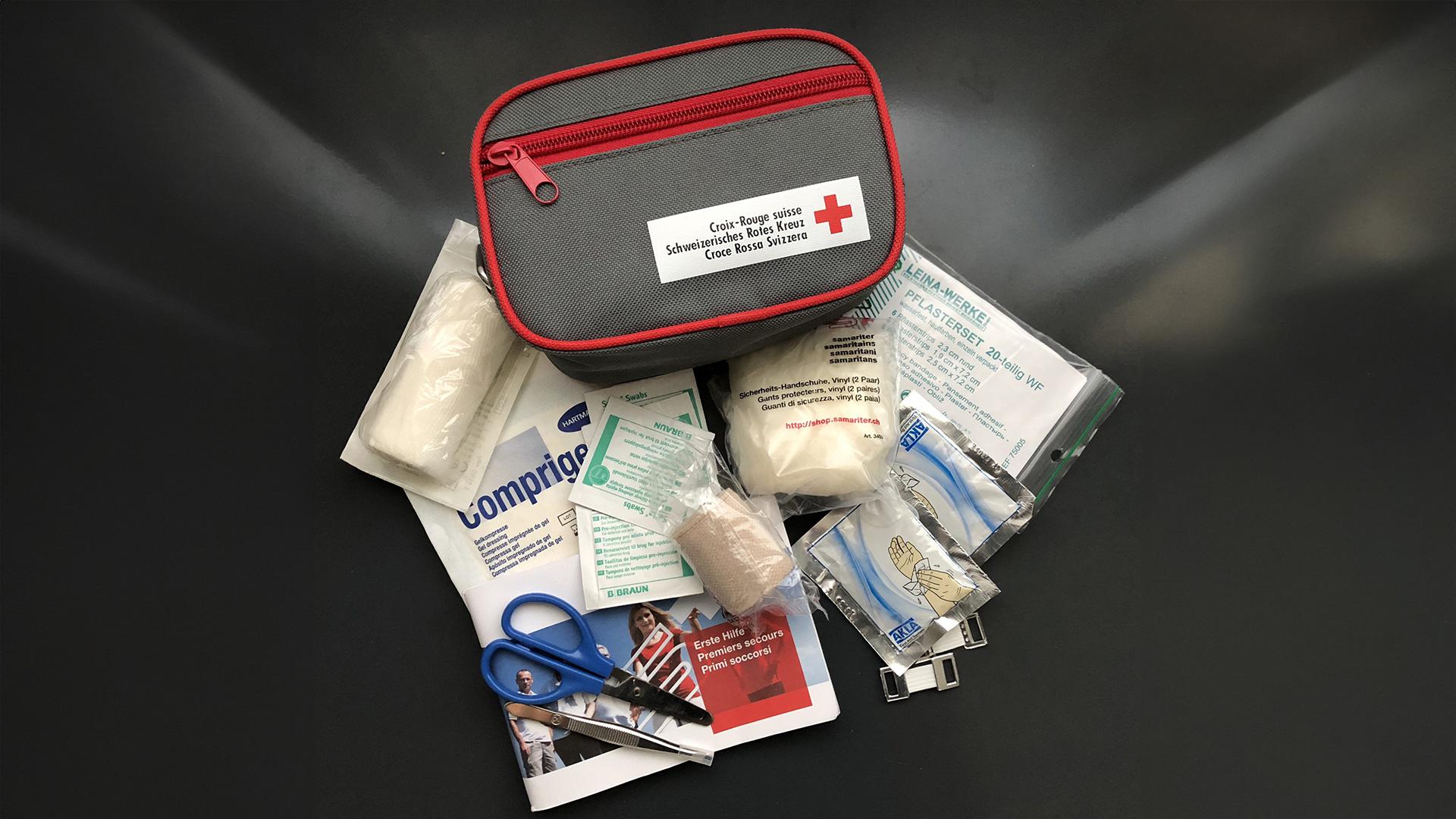 Nothilfeset bestehend aus einer kleinen Tasche mit Verband, Schere, Heftpflaster und weiteren Artikeln für Erste Hilfe. 