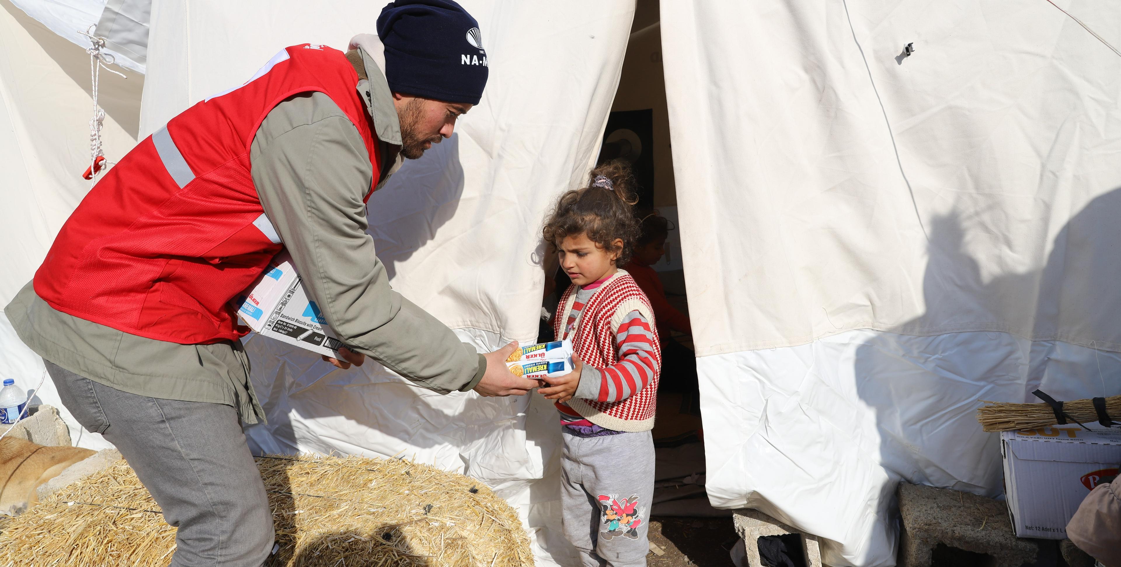 Ein Freiwilliger des Roten Kreuz übergibt einem Kind vor dem Zelt Nahrungsmittel.