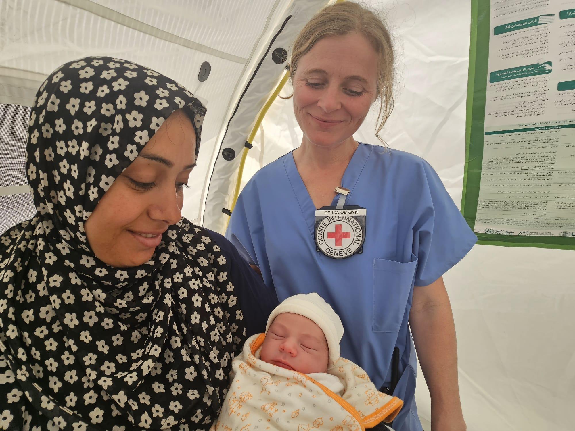Eine Frau hält unter den Augen einer Ärztin ihr Neugeborenes in den Armen.