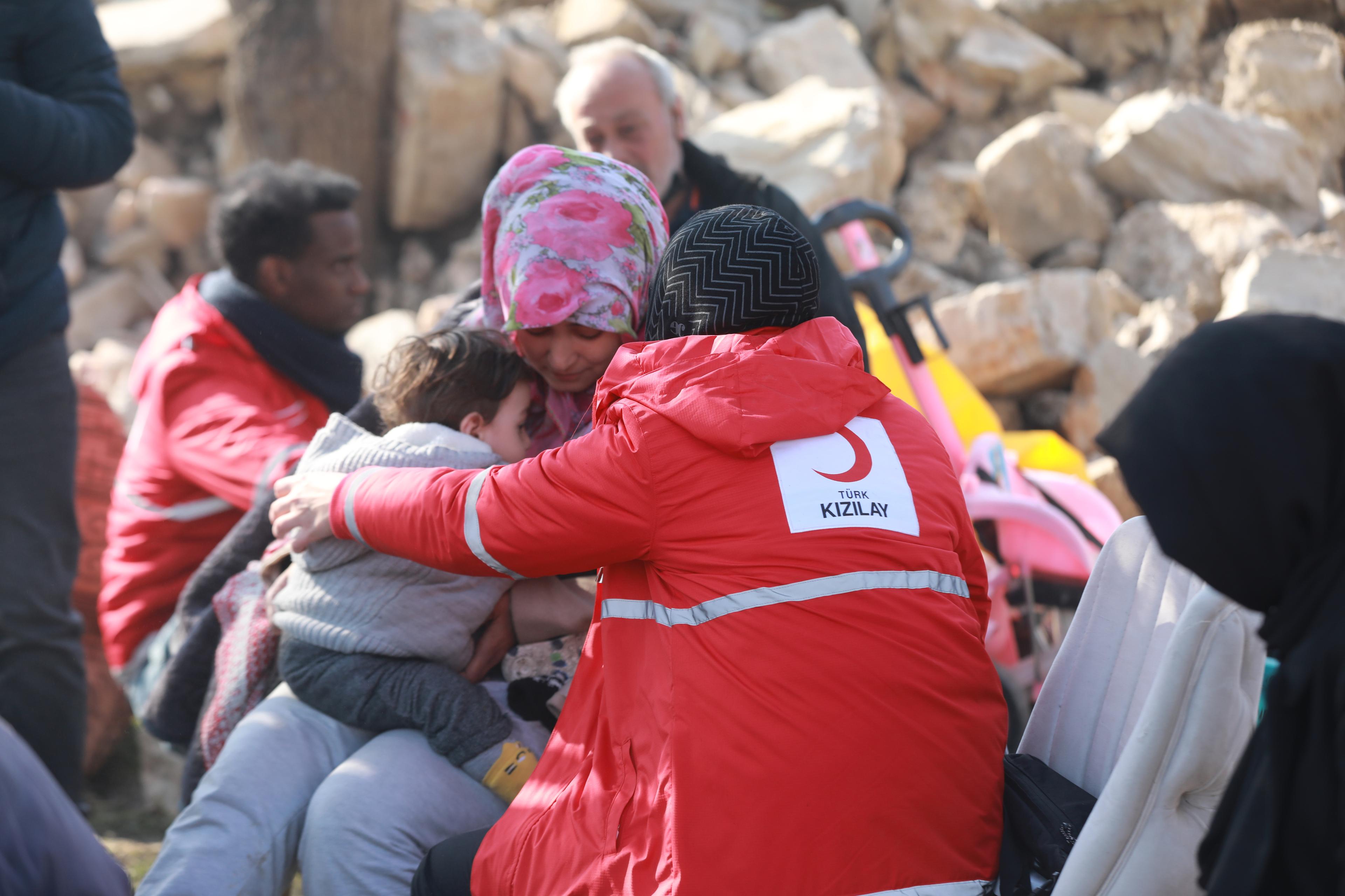 A Turkish Red Crescent worker supports a woman and her child.