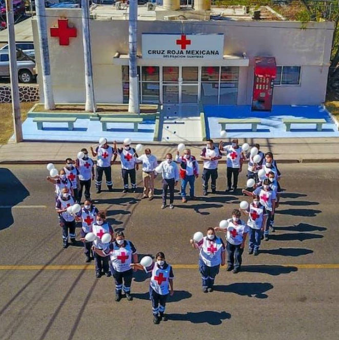 A group of people form a heart formation in front of the Mexican Red Cross building.