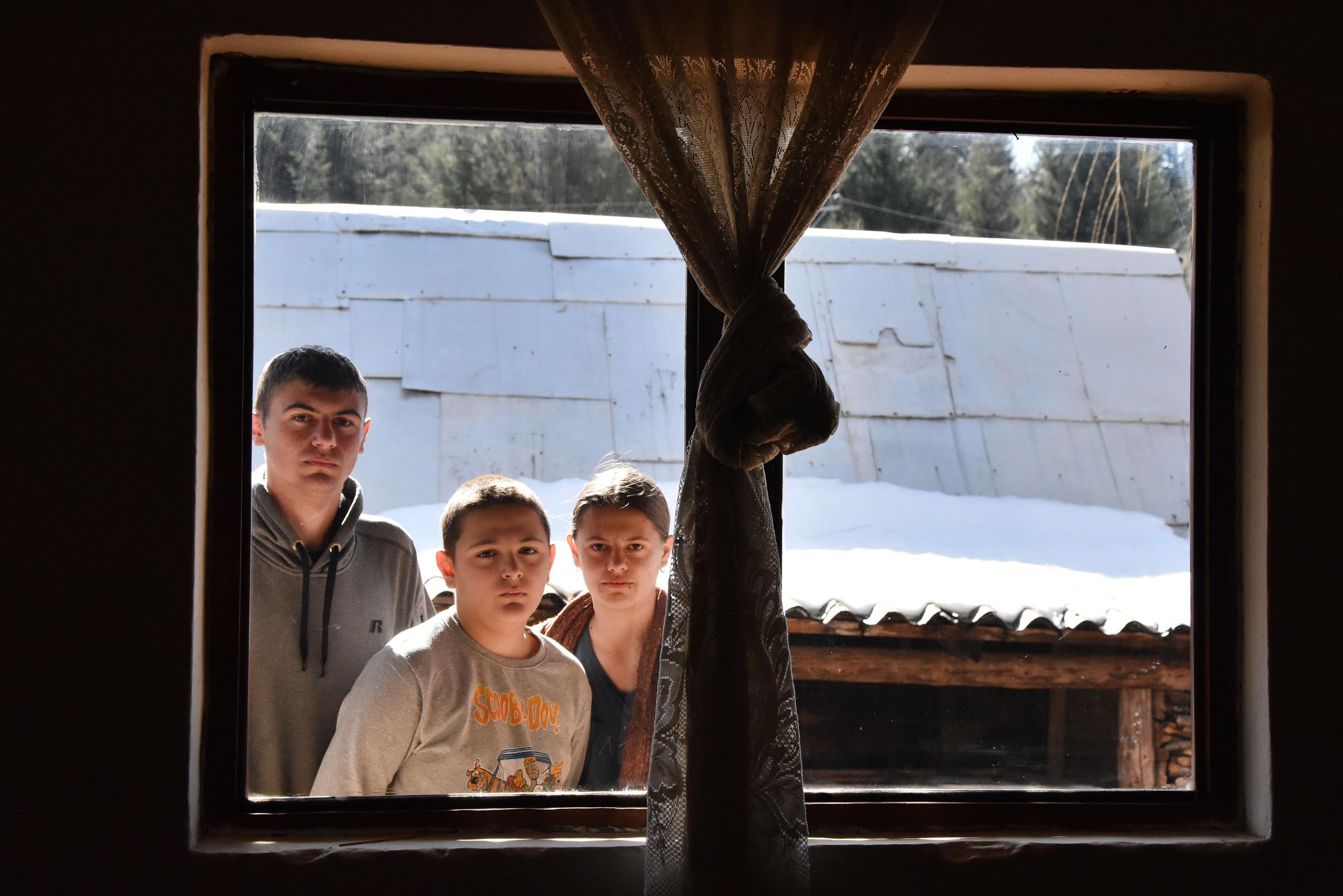 Tre bambini guardano dall'esterno attraverso una finestra