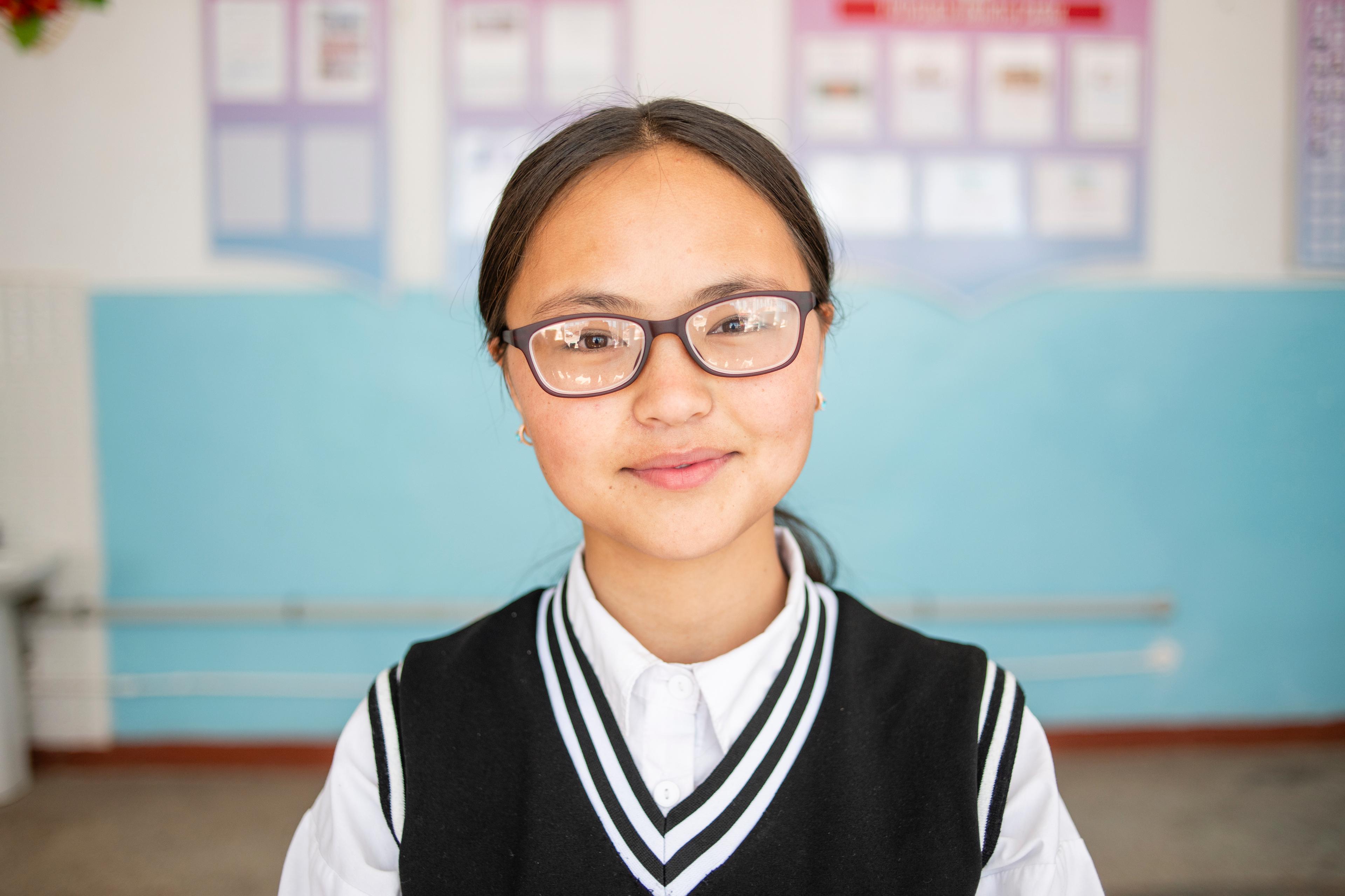 Die 15-jährige Schülerin Bernet Amatova trägt ihre neue Brille und lächelt. 