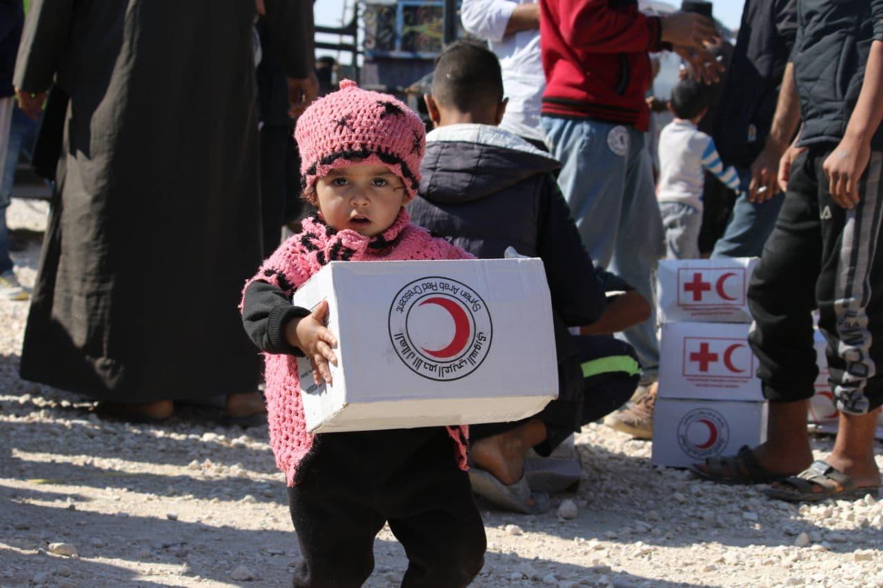 Une jeune fille porte un paquet du Croissant-Rouge arabe syrien.