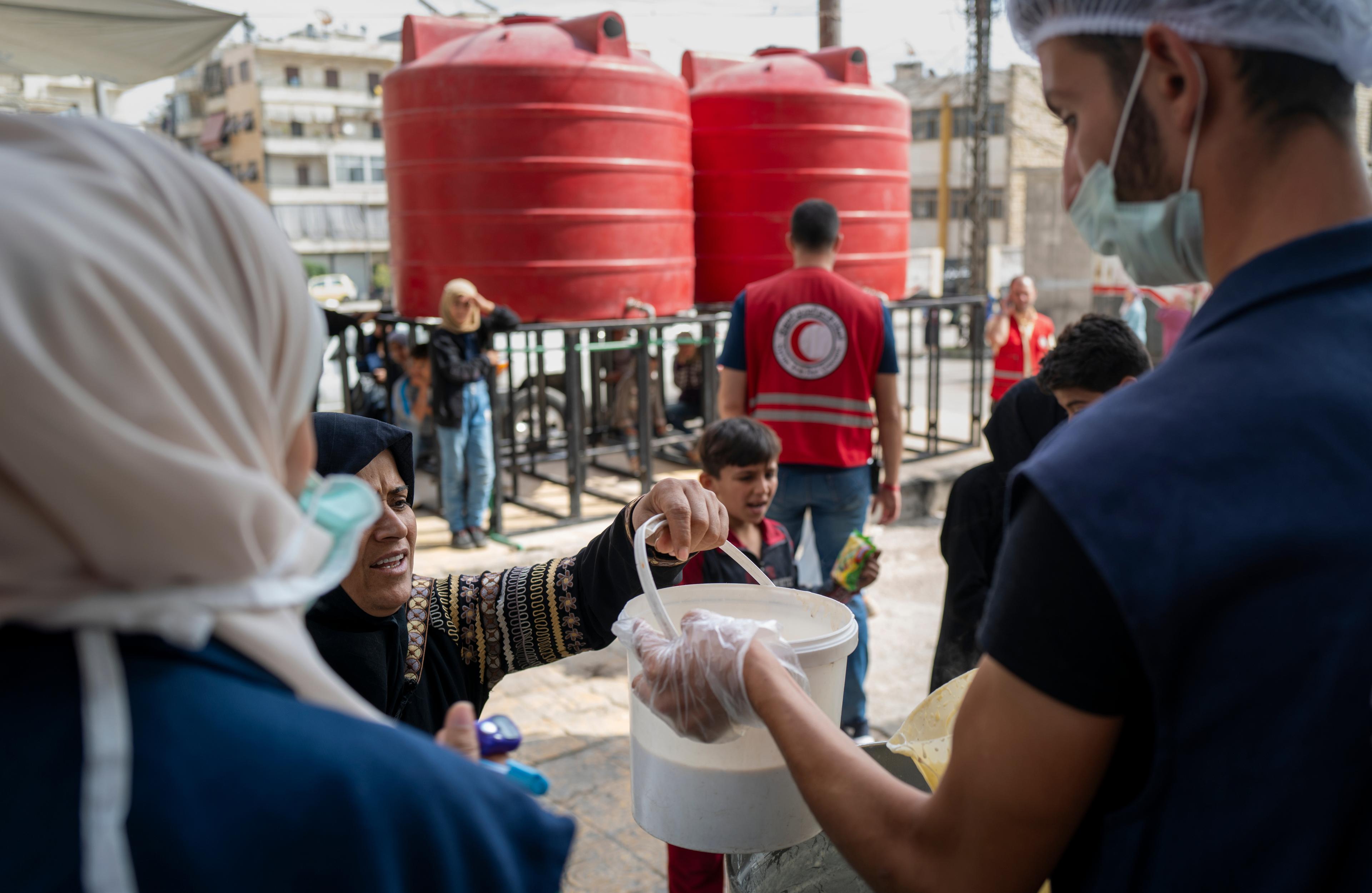 Une femme tend un récipient à un bénévole du Croissant-Rouge arabe syrien lors d'une distribution de nourriture. 