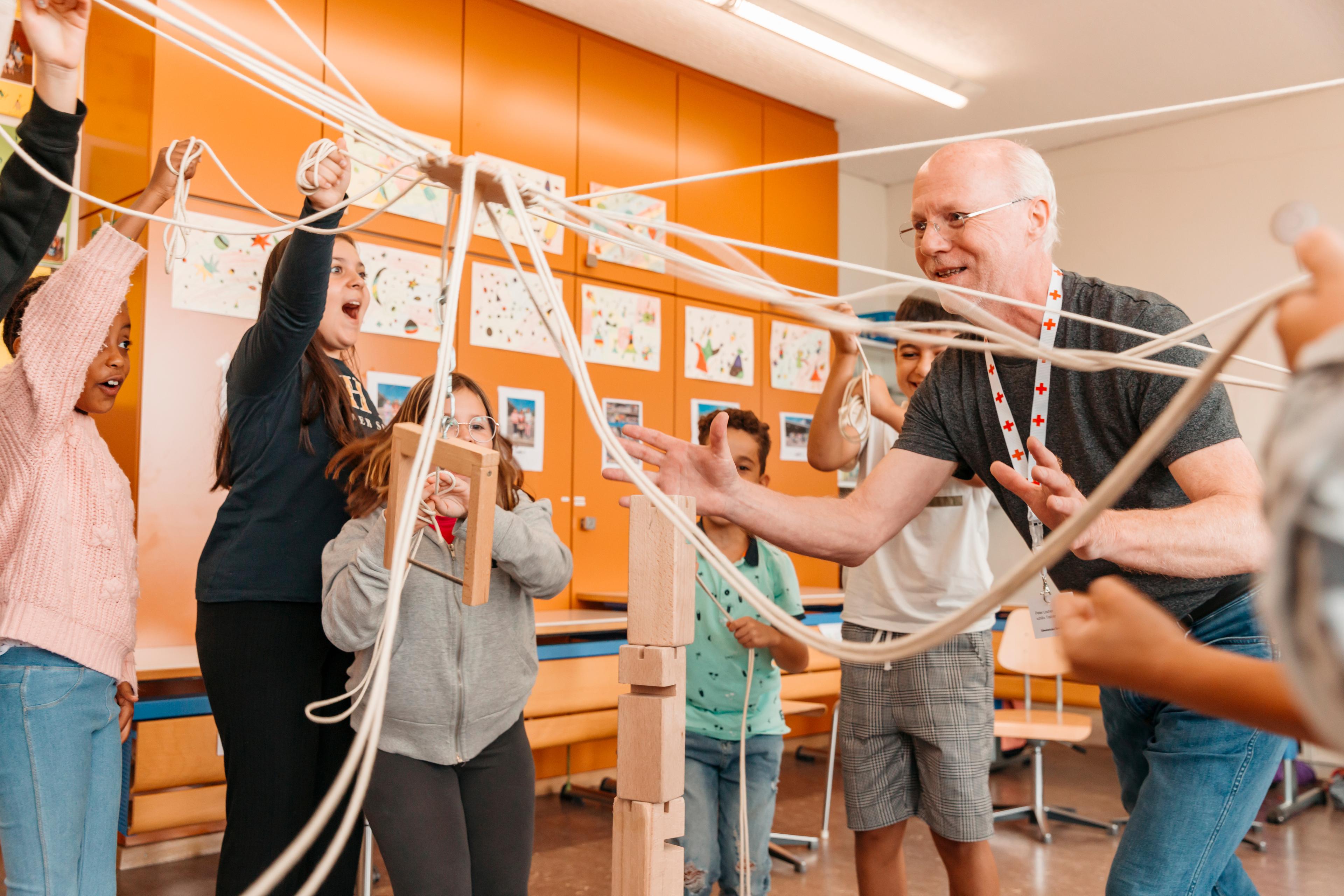 Les élèves font un exercice lors de l’atelier de gestion des conflits chili. Tous en cercle avec le formateur Peter Locher, ils doivent manipuler des cordes pour placer une pièce de bois supplémentaire au sommet d’une tour. 