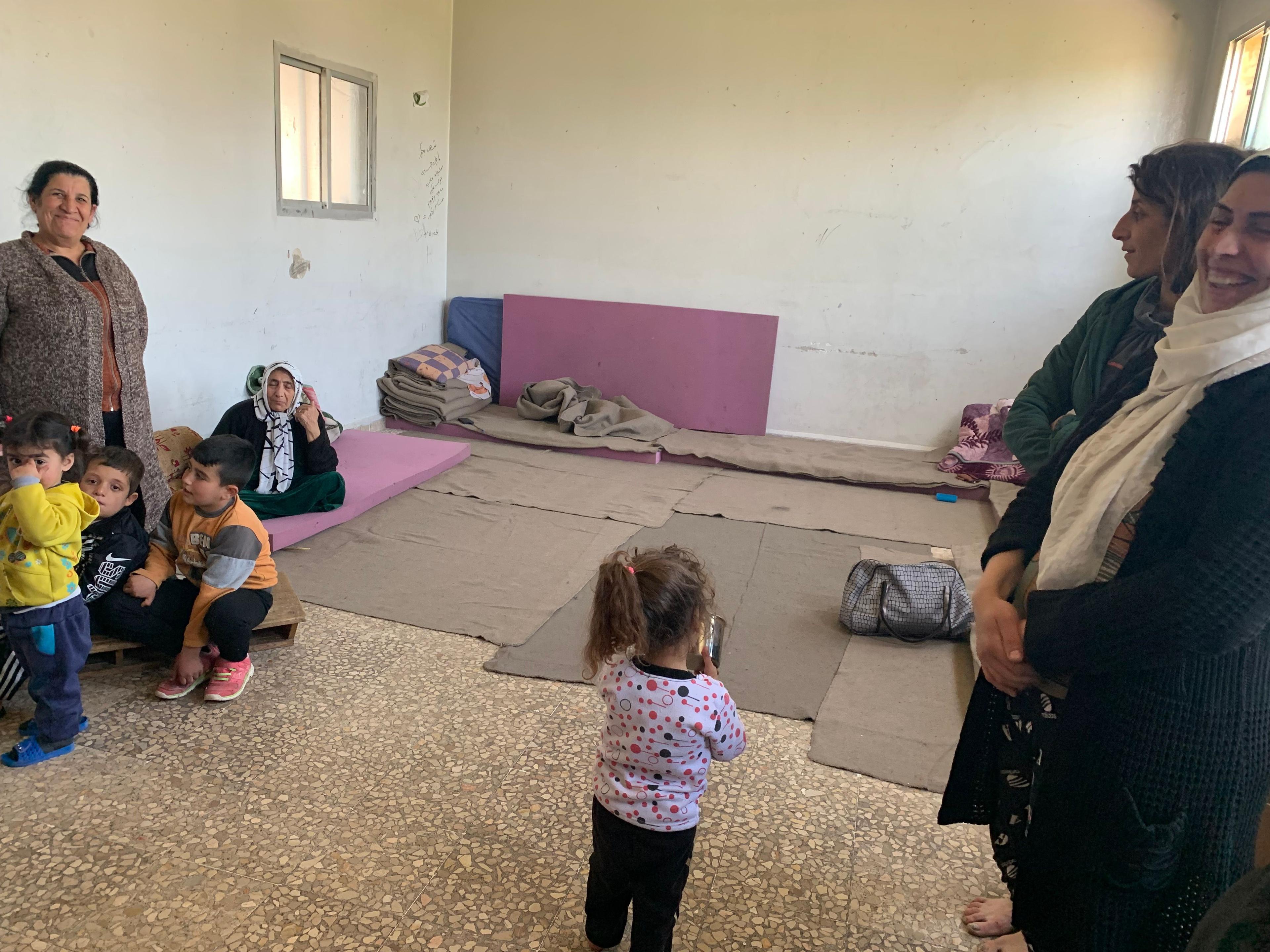 Trois femmes et plusieurs petits enfants sont dans une pièce où l’on voit des matelas et des couvertures.