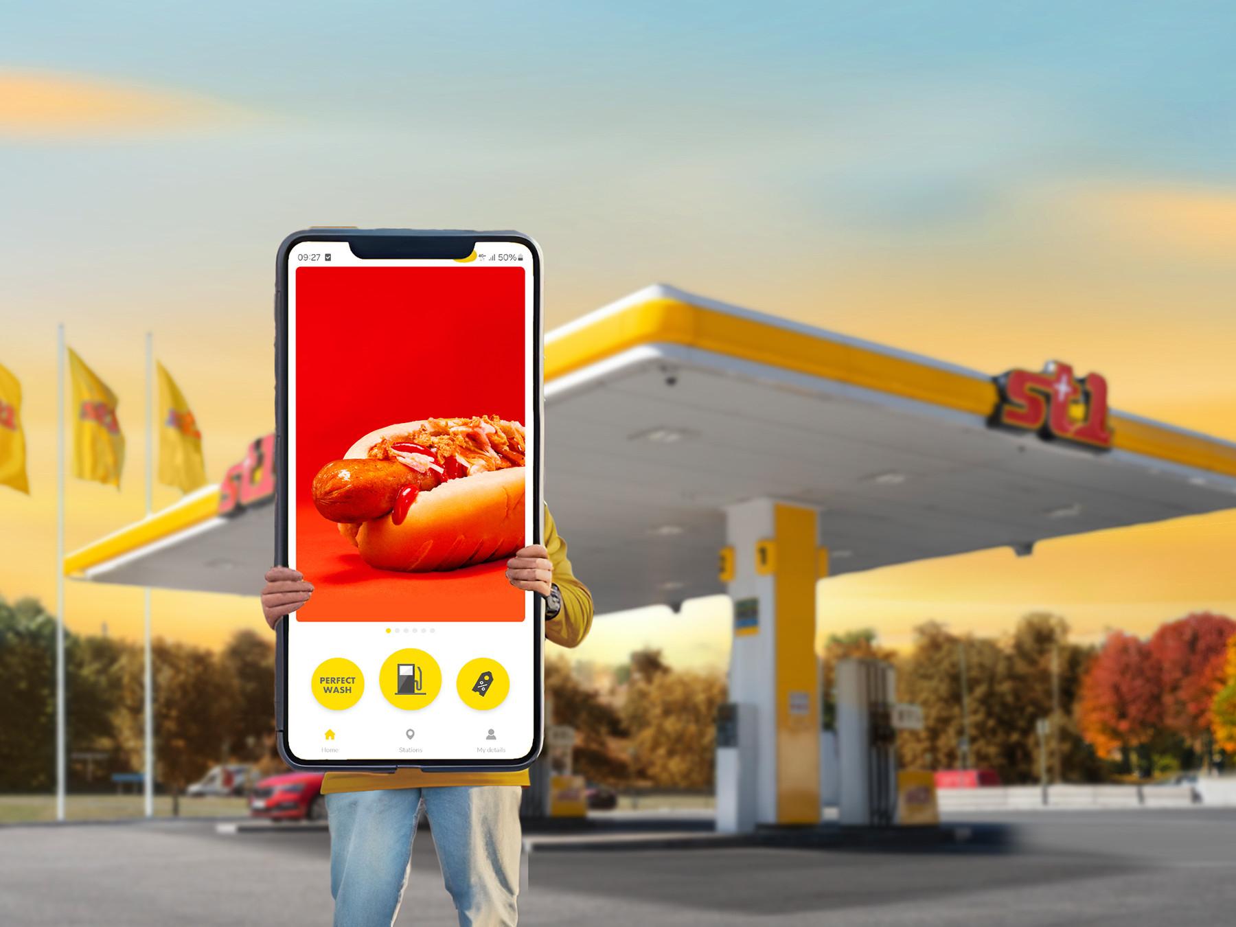 Henkilö kannattelemassa jättikokoista puhelinta St1-huoltoasemalla