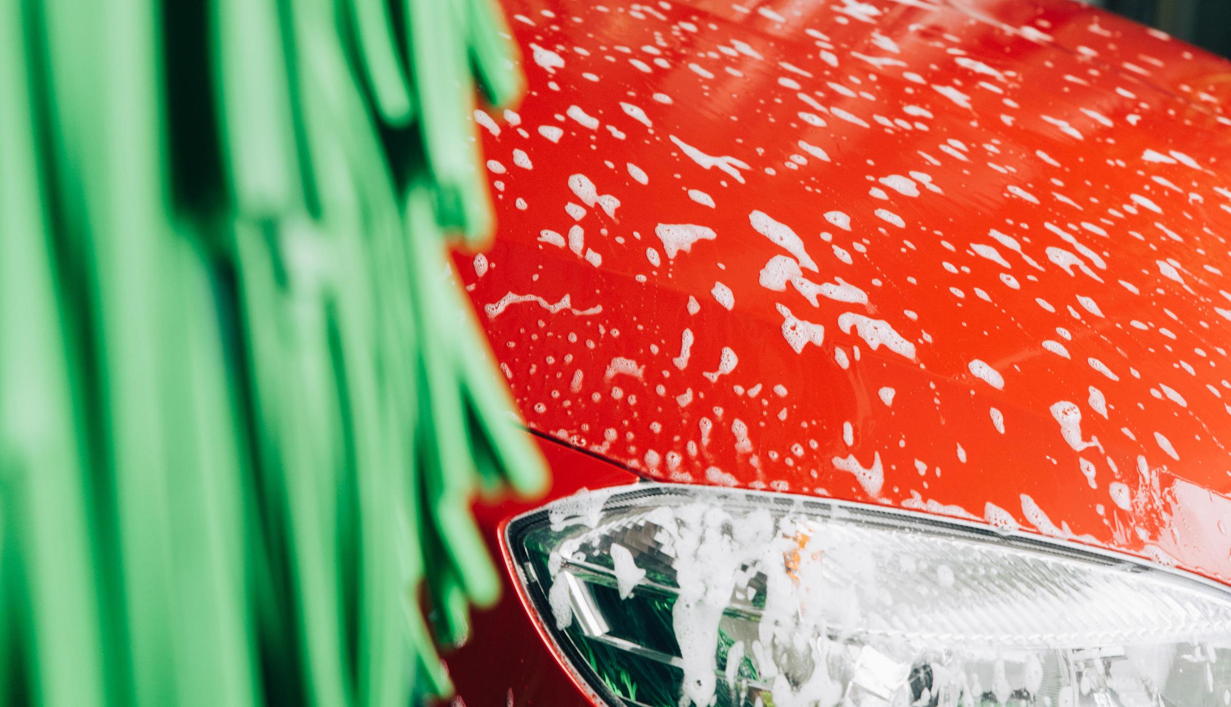 Framflyge av röd bil i biltvätt med skum