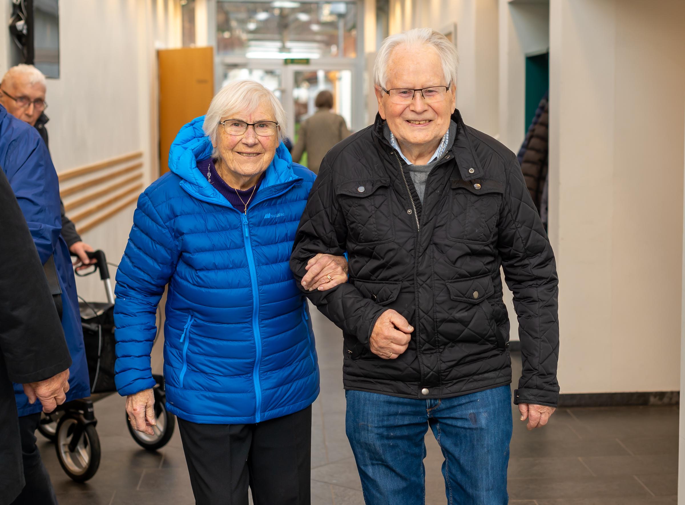 Et eldre ektepar går hånd i hånd i en korridor